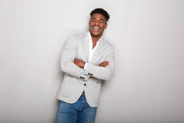 glücklicher junger afroamerikanischer Geschäftsmann lacht mit gekreuzten Armen vor grauem Hintergrund