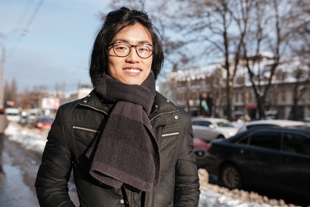 Glücklicher junger asiatischer Mann, der Brille und Schal trägt