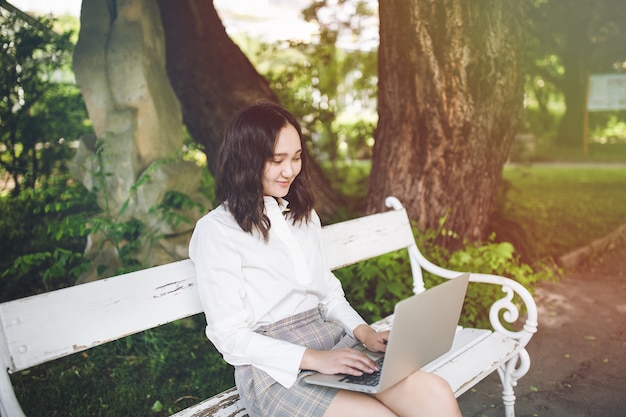 Glücklicher junger asiatischer Student in einem Park, der am Laptop arbeitet