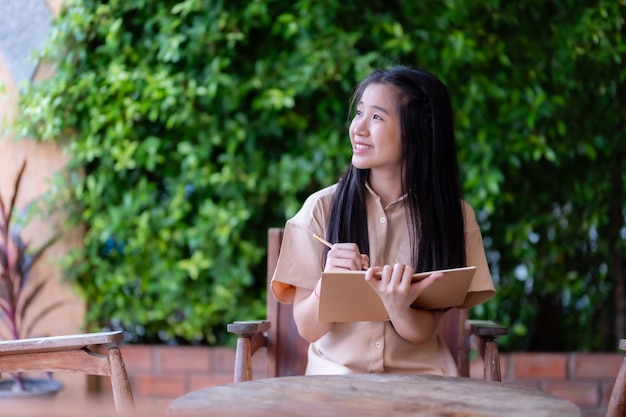 Glücklicher junger asiatischer Teenager-Studentin, die Notizen in ein Notizbuch schreibt.