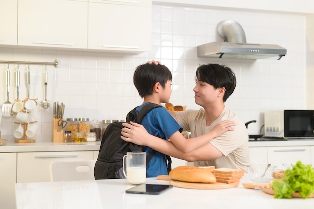 Glücklicher junger asiatischer Vater, der seinen Sohn ermutigt, zur Schule zu gehen