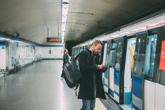 Glücklicher junger blonder Mann mit dem Wandern innerhalb der U-Bahnstation, die auf den Zug wartet
