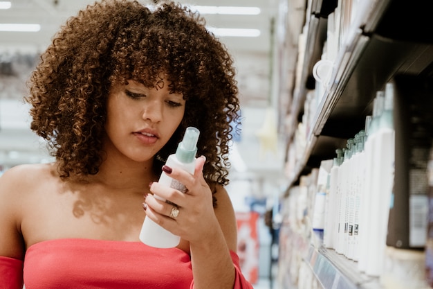 Glücklicher junger Brunette mit kaufendem Shampoo des gelockten Haares im Supermarkt