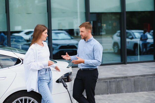 Glücklicher junger erwachsener Mann und lächelnde Frau, die Elektroautos aufladen