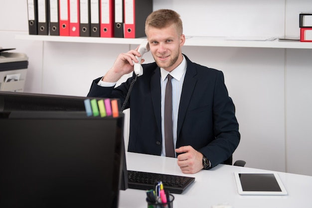 Glücklicher junger Geschäftsmann arbeitet im modernen Büro am Computer