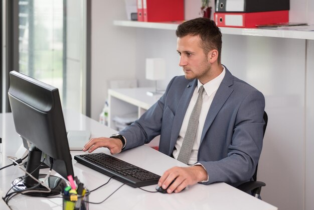 Glücklicher junger Geschäftsmann arbeitet im modernen Büro am Computer