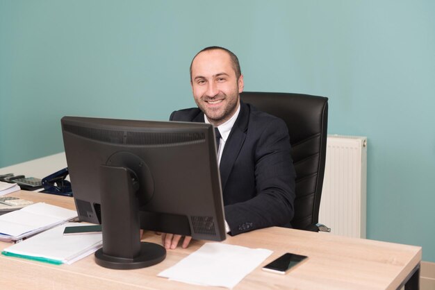 Glücklicher junger Geschäftsmann arbeitet im modernen Büro am Computer