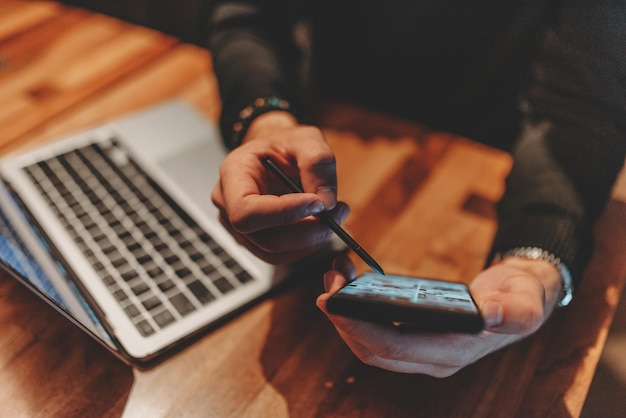 Glücklicher junger Geschäftsmann, der in einem Café an einem Laptop und einem Smartphone arbeitet