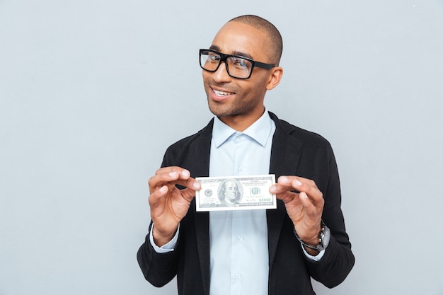 Glücklicher junger Geschäftsmann mit Brille, der Dollar-Banknote lächelt und hält