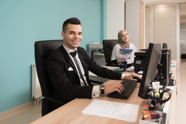 Glücklicher junger Geschäftsmann und muslimische Frau arbeiten im modernen Büro am Computer