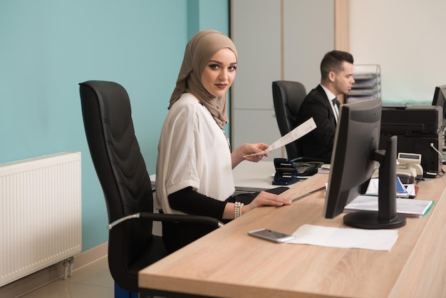 Glücklicher junger Geschäftsmann und muslimische Frau arbeiten im modernen Büro am Computer