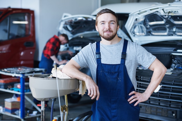 Glücklicher junger Handwerker im blauen Overall, der Sie in der Werkstatt ansieht