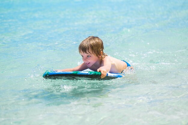 Glücklicher junger Junge des jungen Surfers im Ozean auf Surfbrett