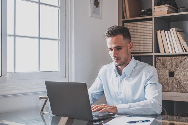 Glücklicher junger kaukasischer Millennial-Geschäftsmann, der zu Hause am Schreibtisch mit Laptop oder Computer arbeitet und sich amüsiert, junger männlicher Mensch in einer Videokonferenz, der sich um das Geschäft oder den Markt kümmert.