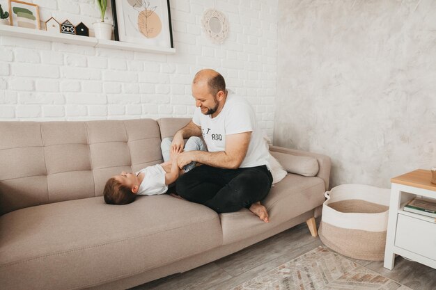 Glücklicher junger kaukasischer Vater auf Sofa im Wohnzimmer, der mit kleinem Vorschulsohn spielt