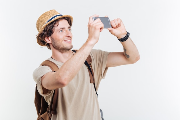 Glücklicher junger lächelnder Mann mit Rucksack, der selfie lokalisiert auf einem weißen Hintergrund macht