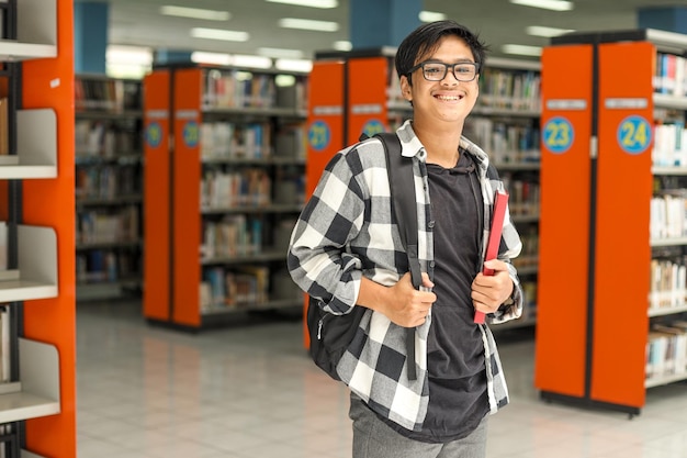 Glücklicher junger männlicher Student, der in der öffentlichen Bibliothek steht, um an einem Studienforschungsprojekt zu arbeiten