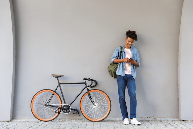 Glücklicher junger Mann, der draußen mit dem Fahrrad geht, das durch Handy plaudert