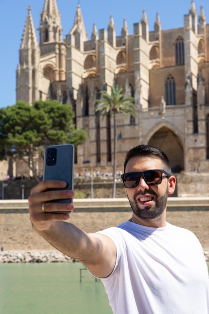 Glücklicher junger Mann, der ein Foto mit seinem Handy in der Kathedrale von Palma de Mallorca in Spanien macht