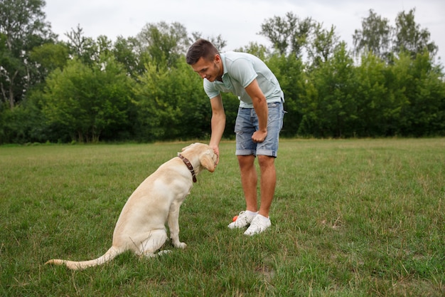 Glücklicher junger Mann, der Hund Labrador im Freien füttert