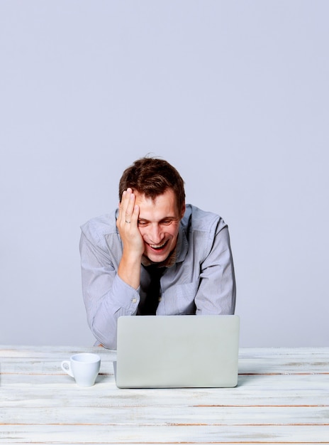 Glücklicher junger Mann, der im Büro auf grauem Hintergrund am Laptop arbeitet