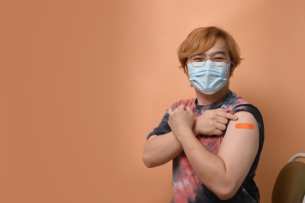Glücklicher junger Mann, der nach der Impfstoffinjektion den Arm zeigt Impfung und Immunisierung