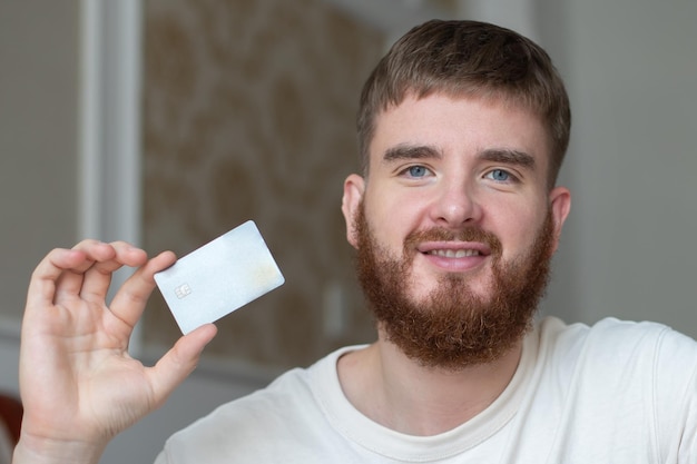 Glücklicher junger Mann hält Kreditkarte in der Hand und nutzt Laptop-Computer lächelnd zu Hause beim Online-Shopping