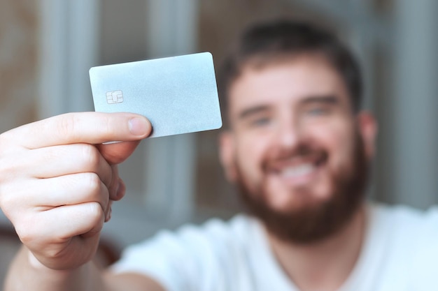 Glücklicher junger Mann hält Kreditkarte in der Hand und nutzt Laptop-Computer lächelnd zu Hause beim Online-Shopping