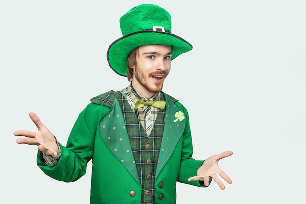 Glücklicher junger Mann in St Patrick Klagenstand und -haltung. Sein Kostüm grün. Isoliert auf grau.