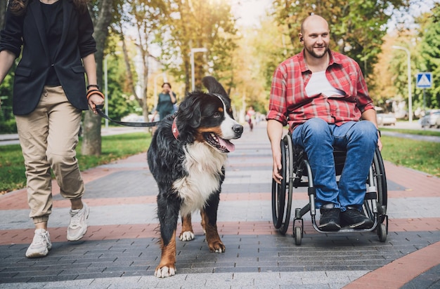 Glücklicher junger Mann mit einer körperlichen Behinderung, der mit seinem Hund einen Rollstuhl benutzt