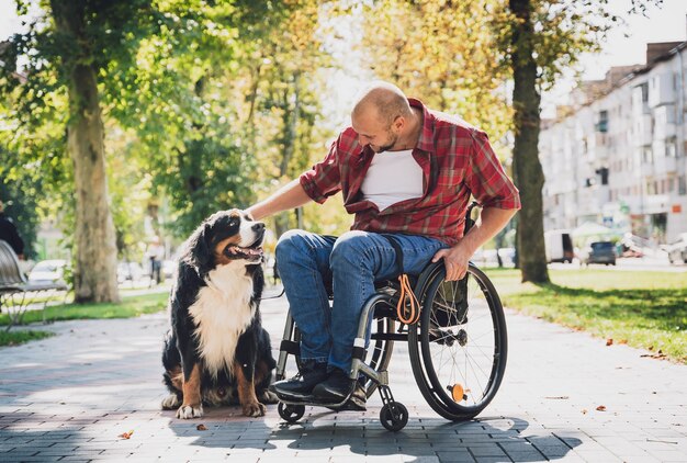 Glücklicher junger Mann mit einer körperlichen Behinderung im Rollstuhl mit seinem Hund