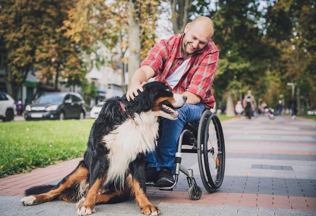 Glücklicher junger Mann mit einer körperlichen Behinderung im Rollstuhl mit seinem Hund