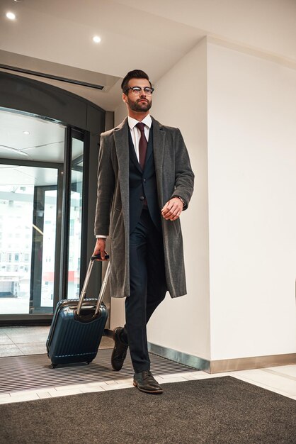 Glücklicher junger Mann mit Reisetasche, der in voller Länge im Hotel spaziert?