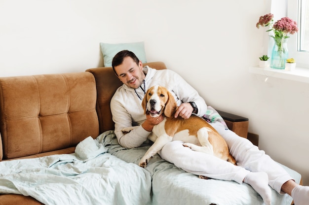 Glücklicher junger Mann mit seinem Hund, Beagle, der auf dem Sofa sitzt.