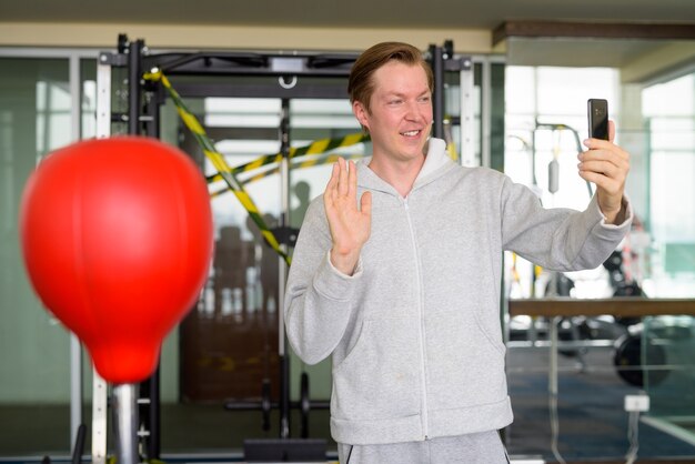 Glücklicher junger Mann Videoanruf und bereit für das Boxen im Fitnessstudio