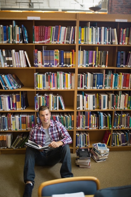 Glücklicher junger Student, der auf Bibliotheksbodenlesung sitzt