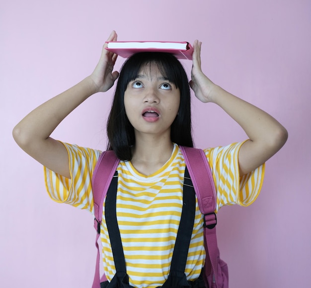 Glücklicher junger Student, der rosa Buch mit Rucksack auf rosa Hintergrund hält.
