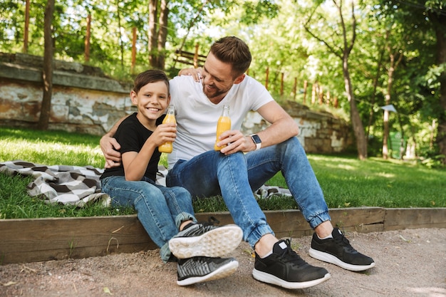 Glücklicher junger Vater, der mit seinem kleinen Sohn draußen sitzt und Saft trinkt.