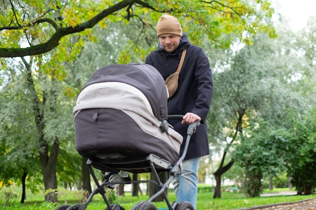 Glücklicher junger Vater mit Kinderwagen während des Spaziergangs in der Natur im Park