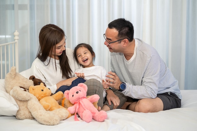 Glücklicher junger Vater und Mutter und eine kleine Tochter spielen mit Spielzeug auf dem Boden sitzend im Wohnzimmer Familienelternschaft und Personenkonzept