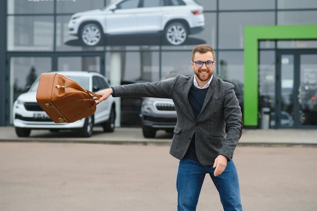 Glücklicher Käufer in der Nähe des Autos vor dem modernen Avtosalon-Gebäude