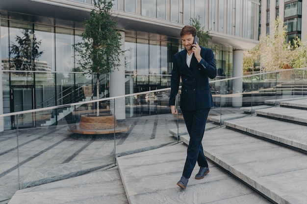 Glücklicher kaukasischer Geschäftsmann, der auf dem Smartphone spricht, während er durch das Bürozentrum geht