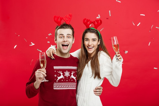 Glücklicher kaukasischer Mann und Frau in den Renhüten das Weihnachten feiern, das mit den Sektkelchen, beglückwünschend auf Weihnachten röstet.