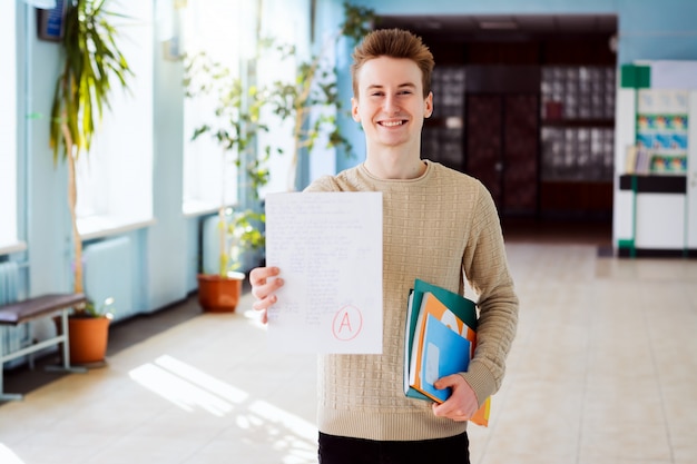 Glücklicher kaukasischer Student hält überprüftes Papier mit Endprüfung mit Grad A