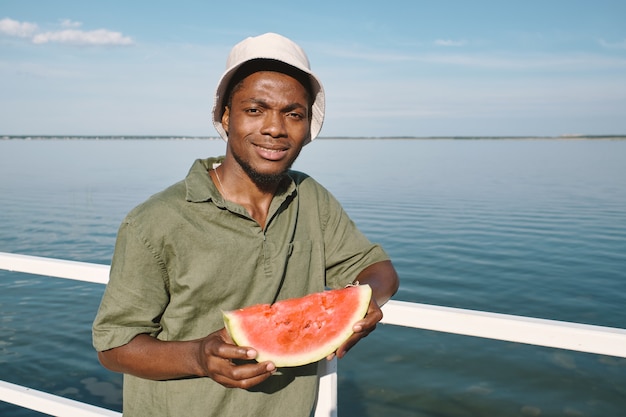 Glücklicher Kerl afrikanischer Abstammung, der ein Stück saftige Wassermelone hält