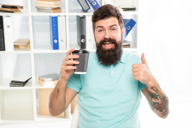 Glücklicher Kerl, der Daumengeste mit Kaffeetasse zum Mitnehmen im Büro gibt, Pause.