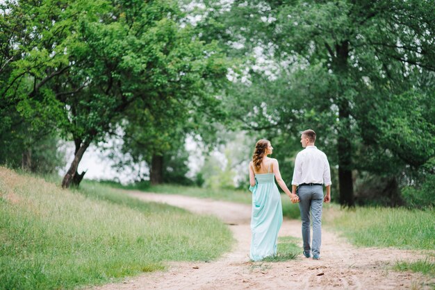 Glücklicher Kerl in einem weißen Hemd und eine Frau in einem türkisfarbenen Kleid, die im Waldpark spazieren geht walking