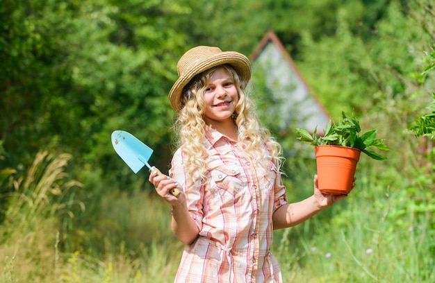 Glücklicher Kindertag Glückliche Kindheit Kind in Hut mit Schulterblatt kleine Schaufel Hacke Glücklich lächelndes Gärtnermädchen Ranchmädchen Pflanzenpflanzen Kleines Kind hält Blumentopf Spring Country Works