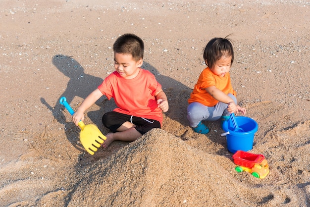 Glücklicher kleiner fröhlicher Bruder und Schwester zwei Kinder lustiges Graben spielen Spielzeug mit Sand am Strand