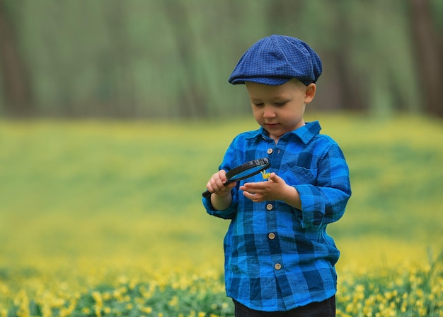 Glücklicher kleiner glücklicher Junge, der die Natur mit einem Lupensommerkonzept von Kind und Natur erkundet